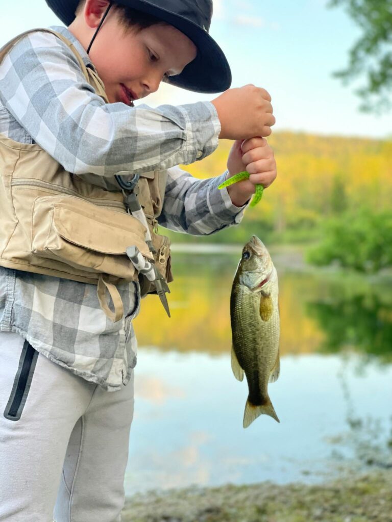 A young boy proudly displays his fish catch during a summer day at a scenic lake.
