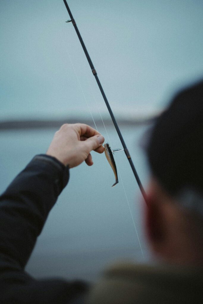Close-up of a person holding a fishing rod with a lure over a calm water backdrop.