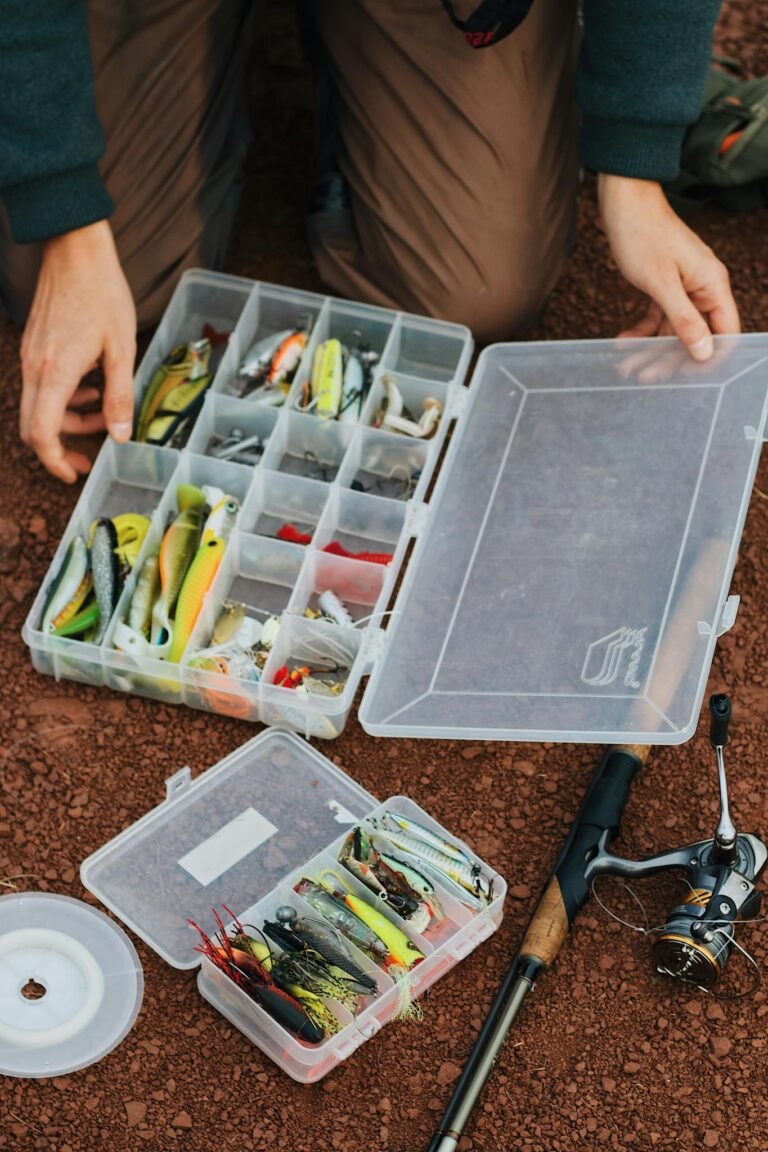 Fisherman arranging fishing lures in a tackle box beside a fishing rod.