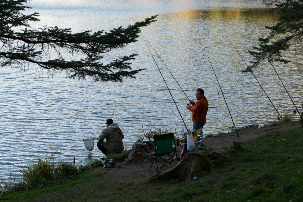Two men fishing by a tranquil lake, enjoying nature and solitude in the evening light.