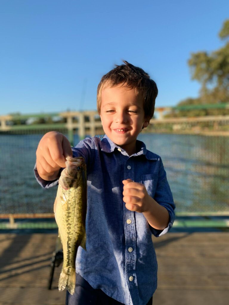 Young boy proudly displays his catch during a sunny day fishing on a pier in Lodi, California.